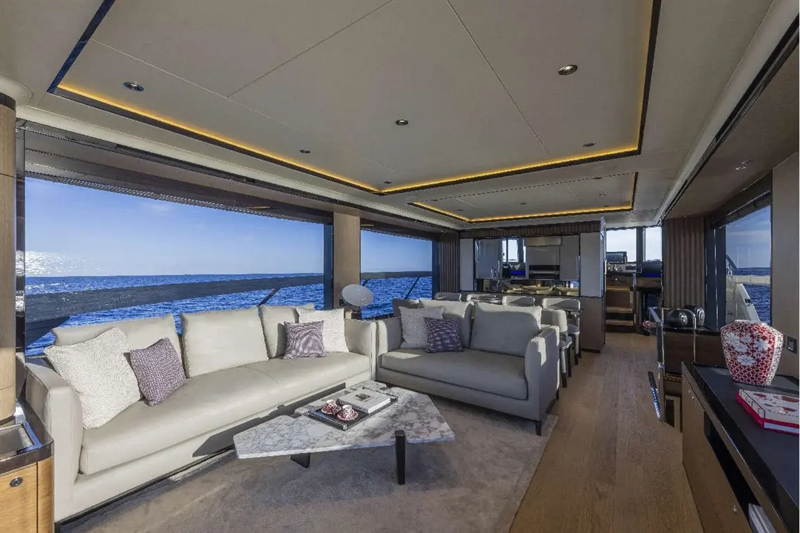 Luxurious yacht interior with cream sofas, a marble table, and panoramic ocean views. Bright, modern design elements throughout.
